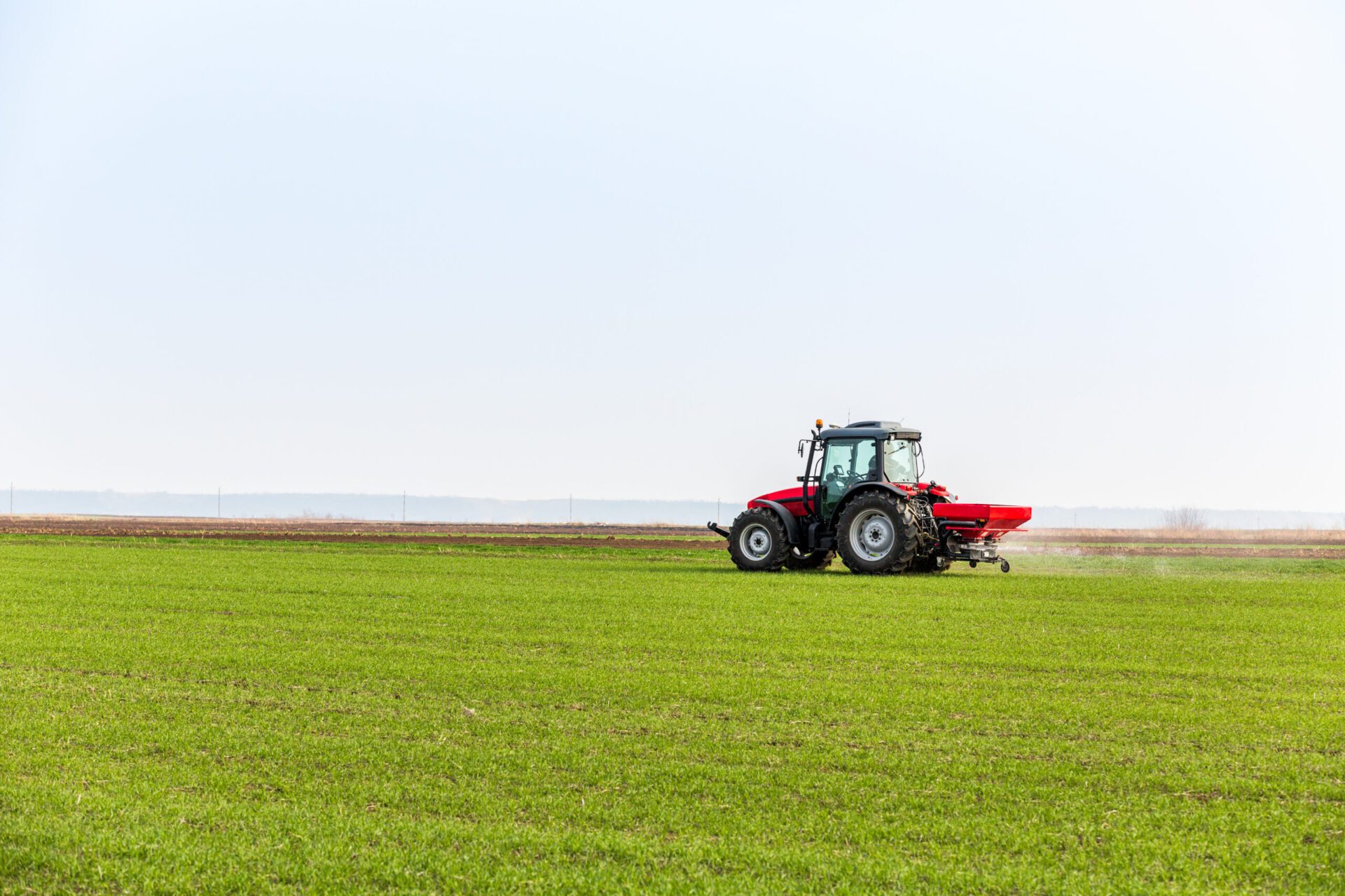 farmer in tractor fertilizing wheat field at spring with npk