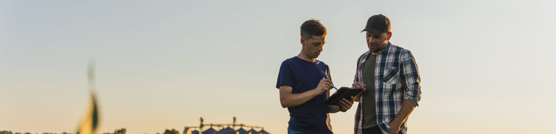 male farmer and agronomist using digital tablet while standing in corn field against sky